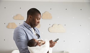 father holding baby in nursery on cell phone