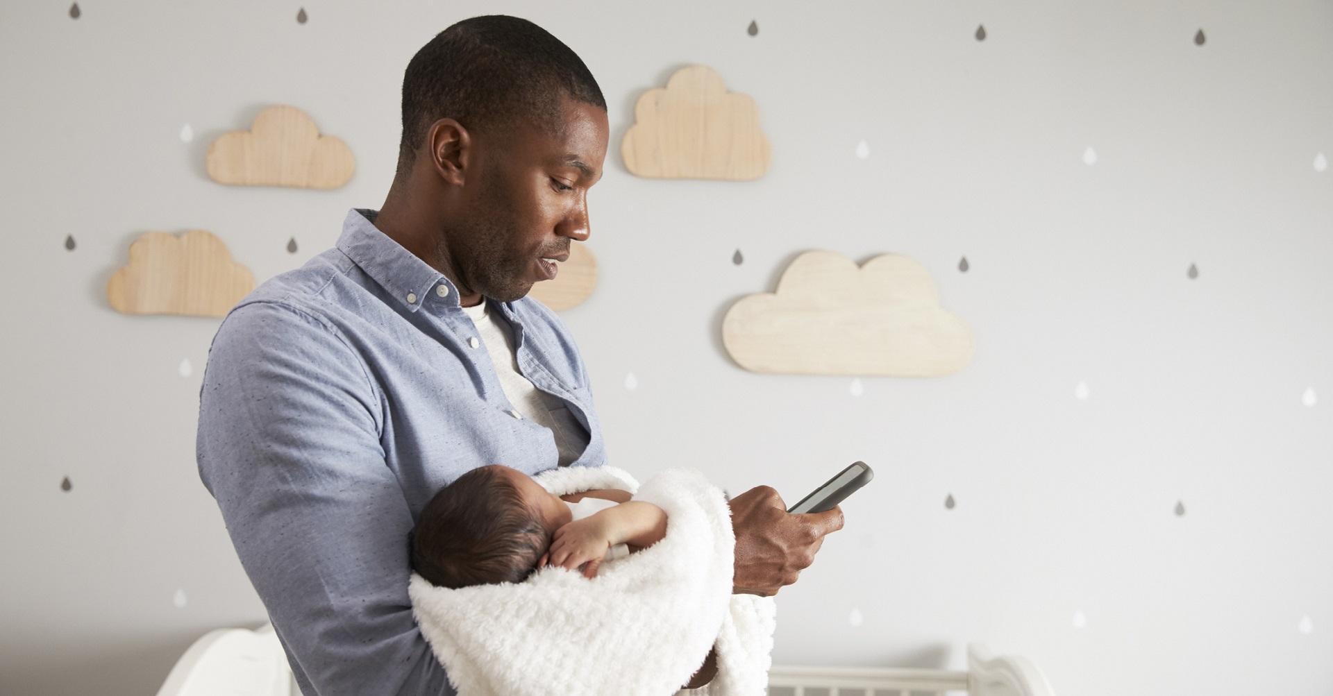 father holding baby in nursery on cell phone
