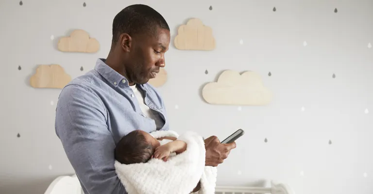 father holding baby in nursery on cell phone