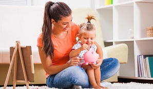 mother putting money in piggy bank with daughter