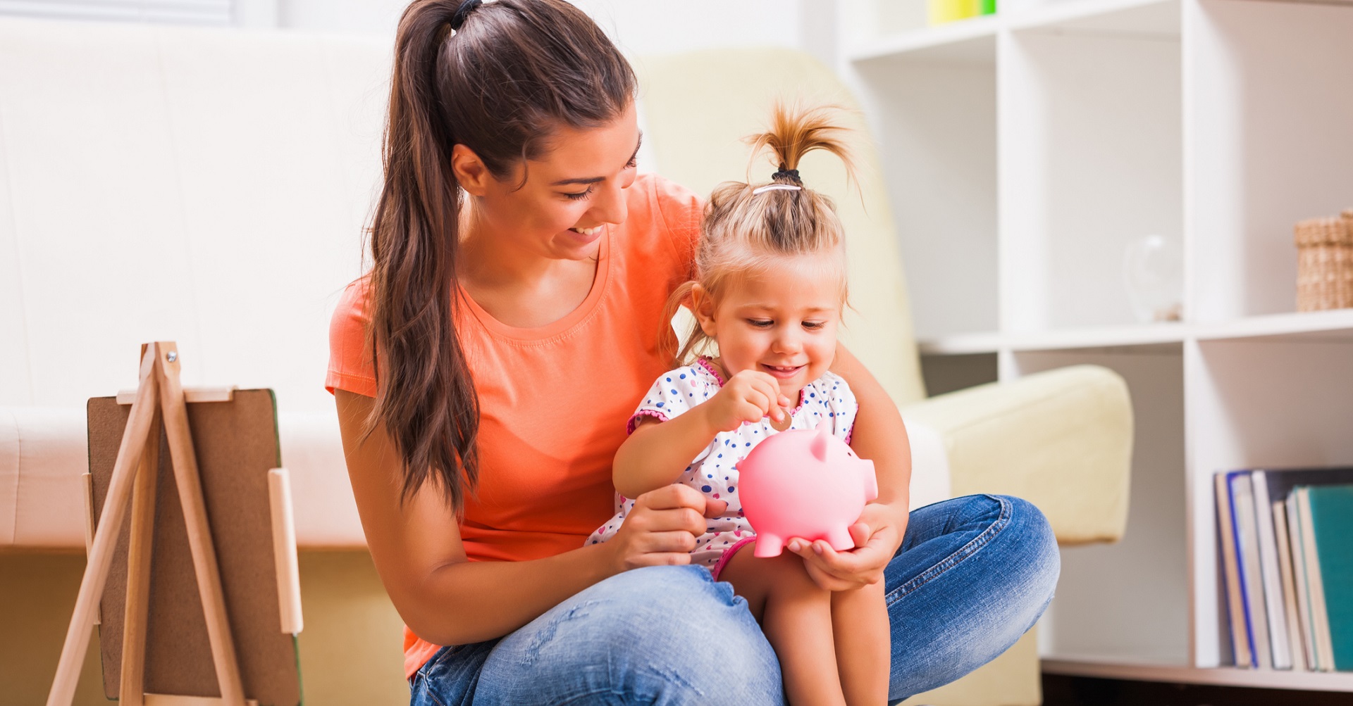 mother putting money in piggy bank with daughter