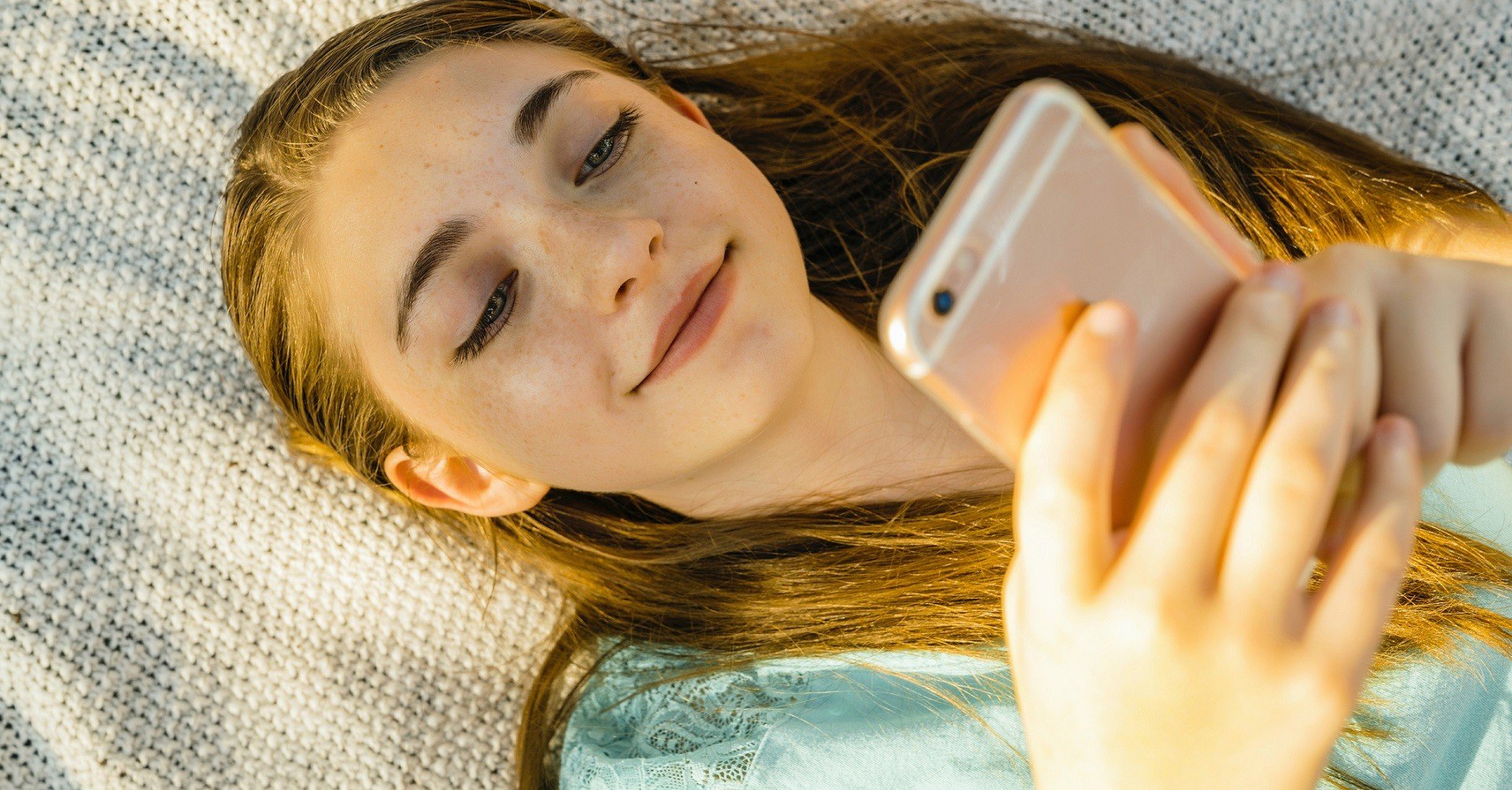 Young girl laying down playing on cellphone