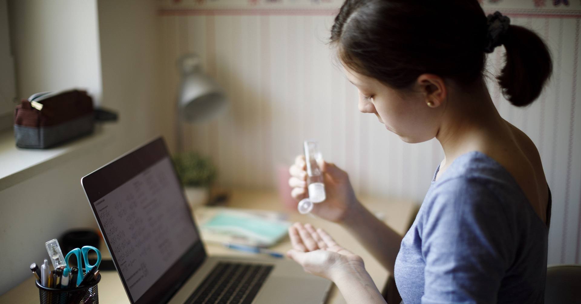 Girl sitting at desk using hand sanitizer