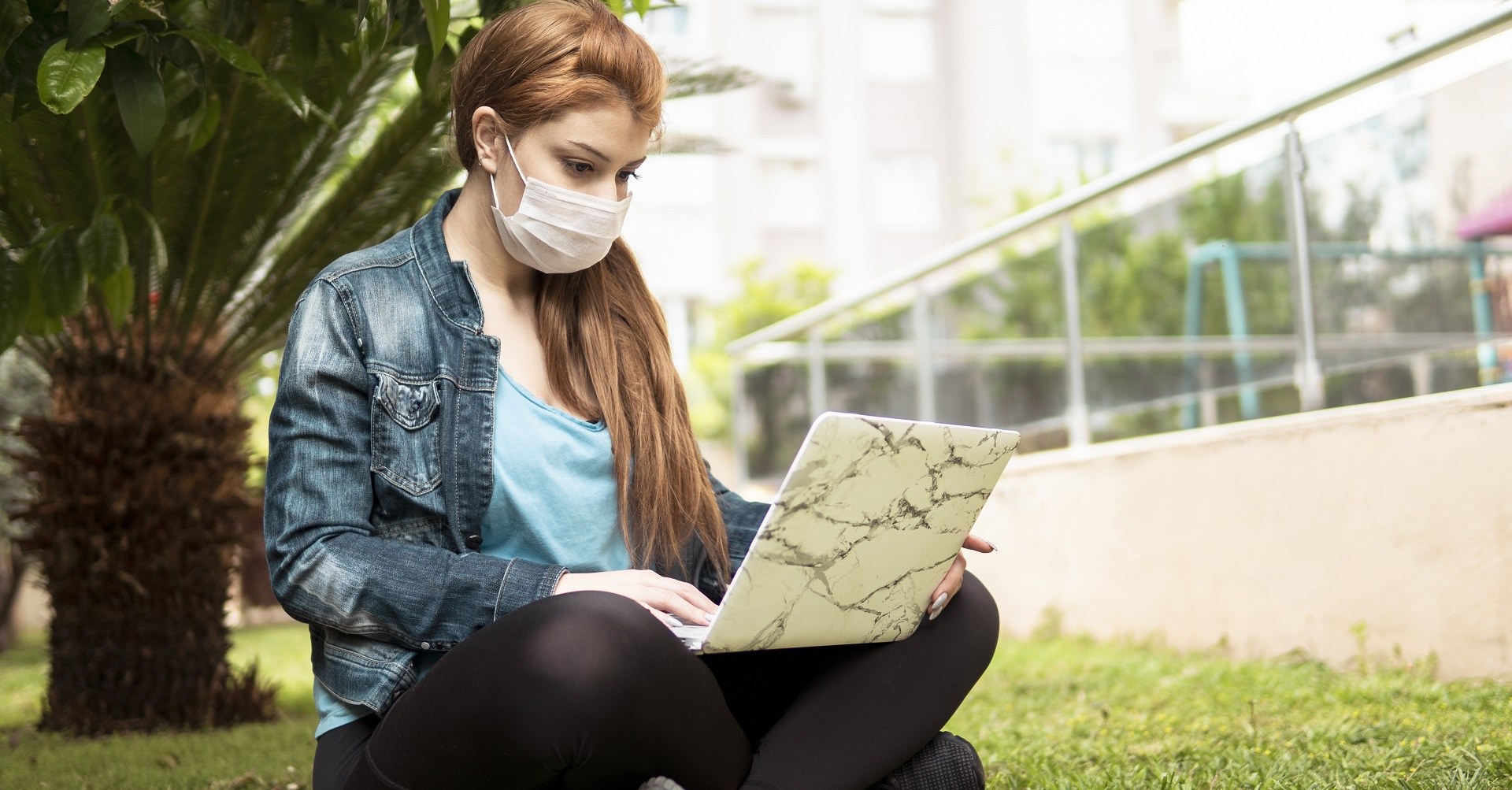 Woman sitting on lawn on laptop with face mask