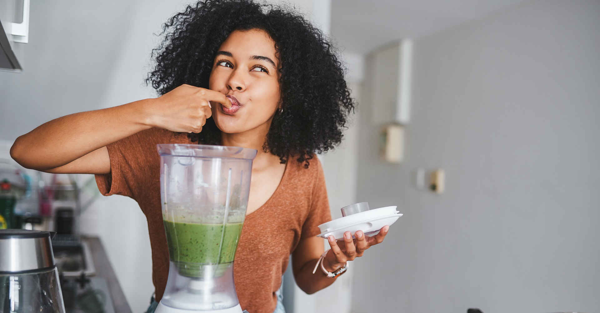 Woman tasting mixture from blender