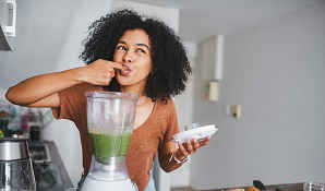 Woman tasting mixture from blender