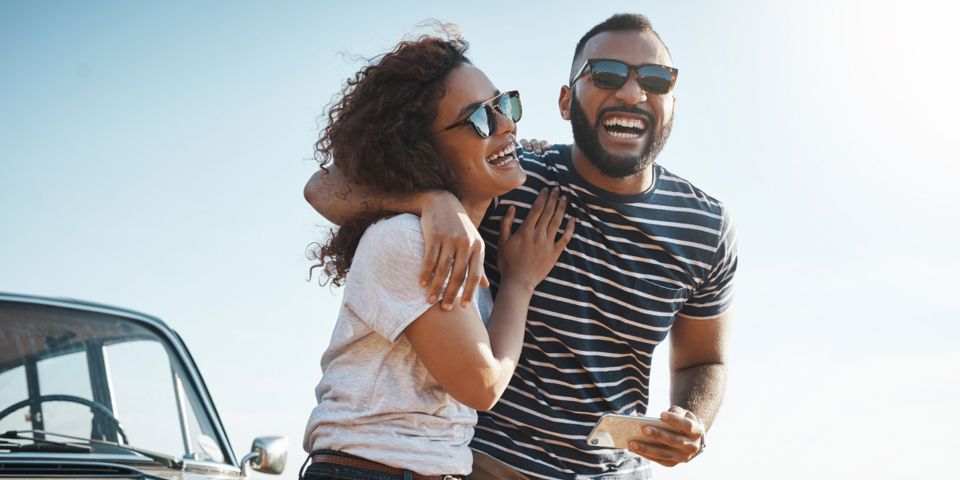 Couple sitting on bonnet of car smiling