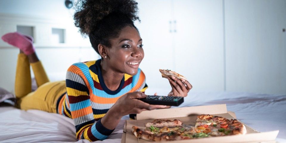 Woman eating pizza on her bed 