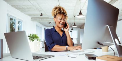 woman sitting at computer desk talking on mobile