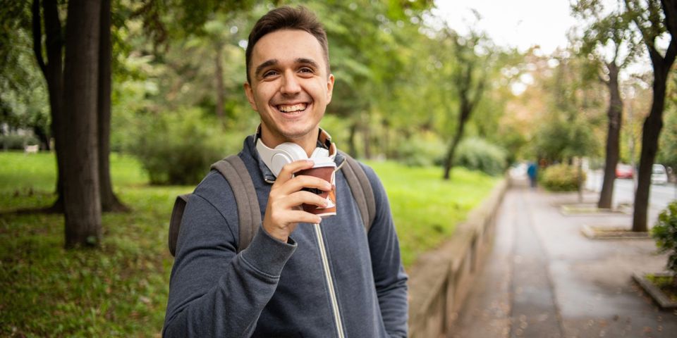 man in park holding up a coffee