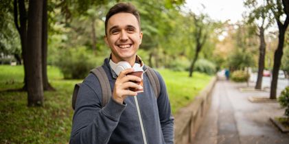 man in park holding up a coffee
