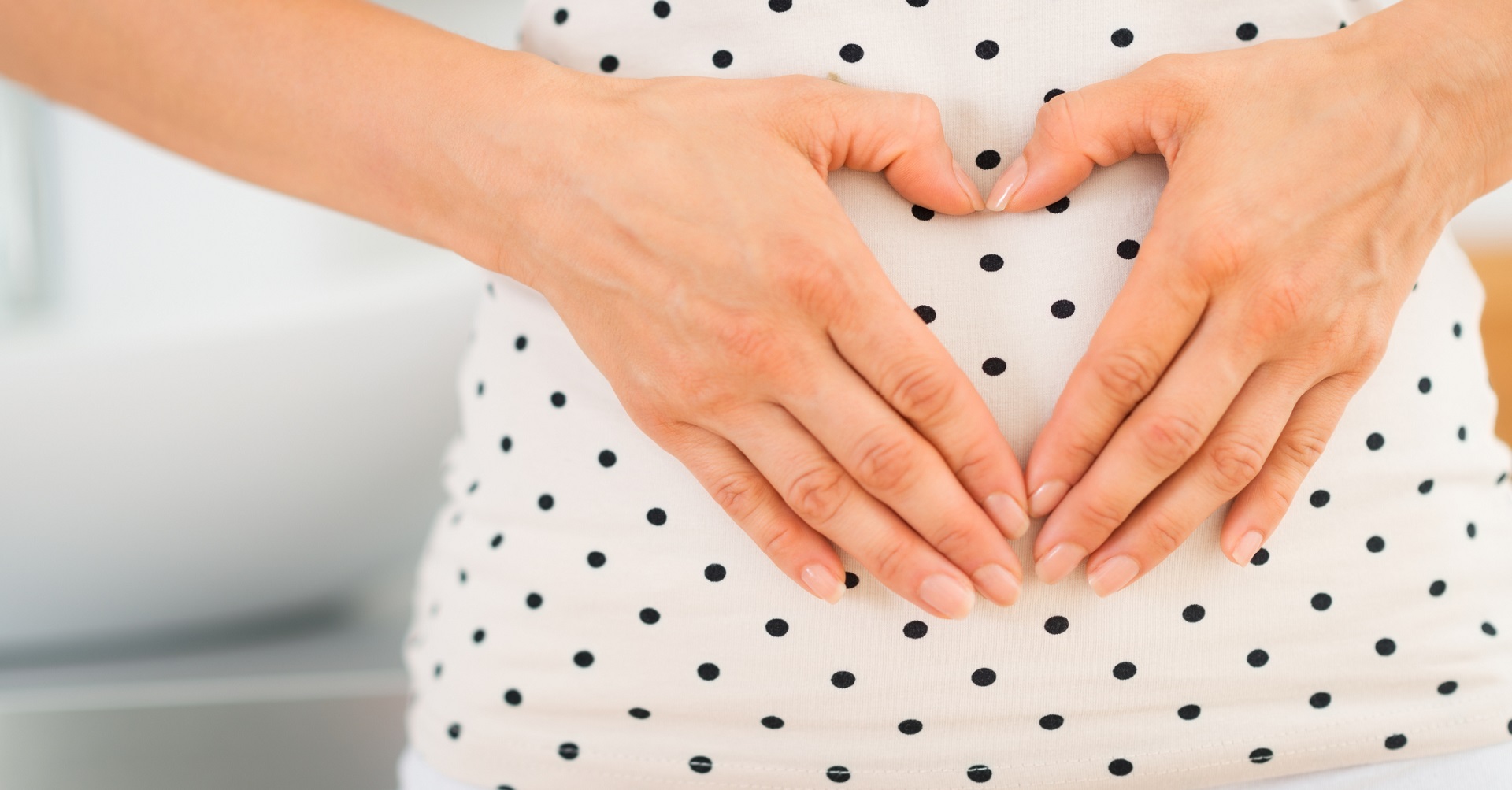 Woman with hands in heart shape in front of stomach