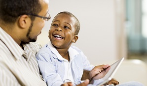 father sitting with child on couch looking at tablet