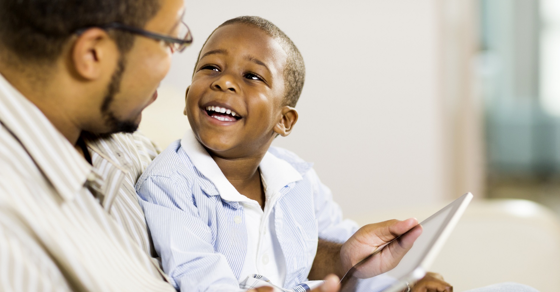 father sitting on couch with son and tablet on his lap