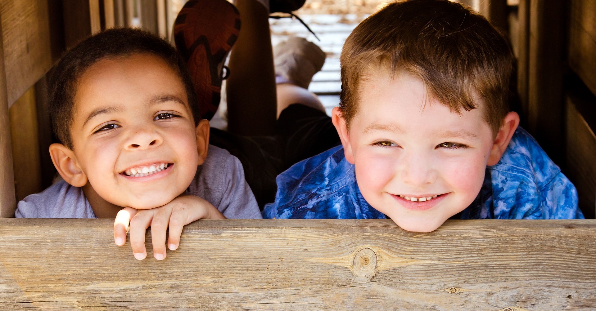 young boys lying behind piece of wood