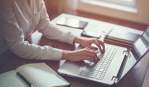 woman on laptop with notepad next to her