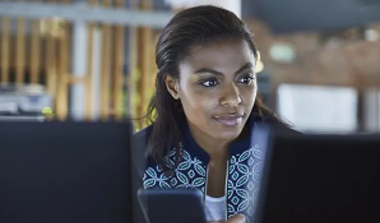 woman holding phone and looking at laptop