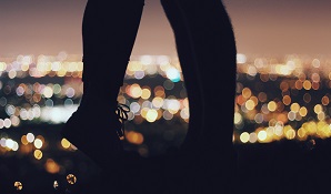 couple standing on cliff with lights behind them