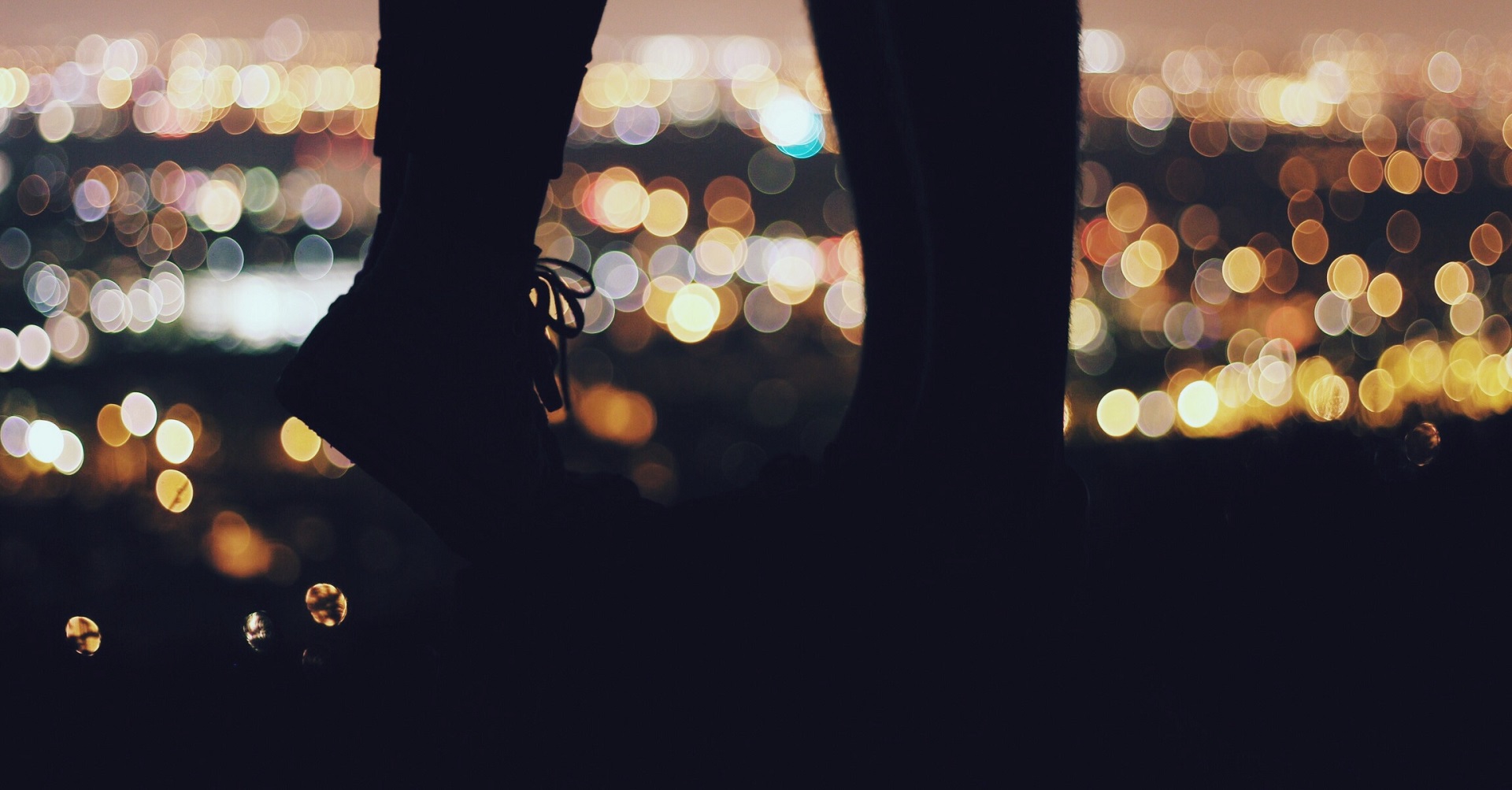 couple standing on cliff with lights behind them