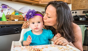 mother kissing baby that has made a mess with food