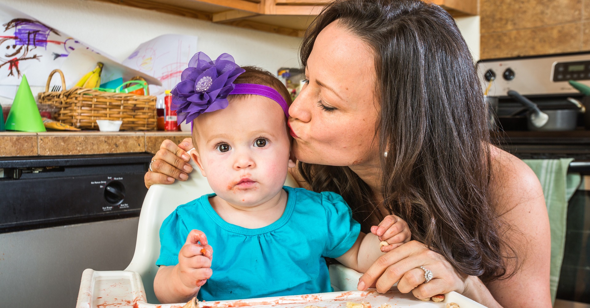mother kissing baby that has made a mess with food