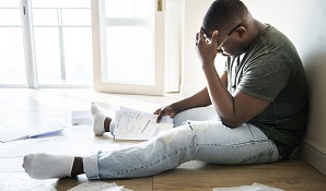 man sitting on the floor looking at all his bills