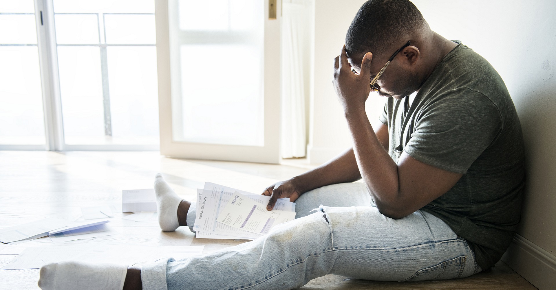 man sitting on the floor looking at all his bills