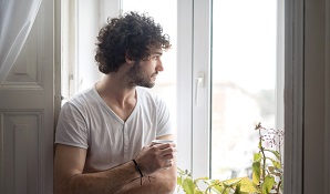 man staring out window with cup of coffee