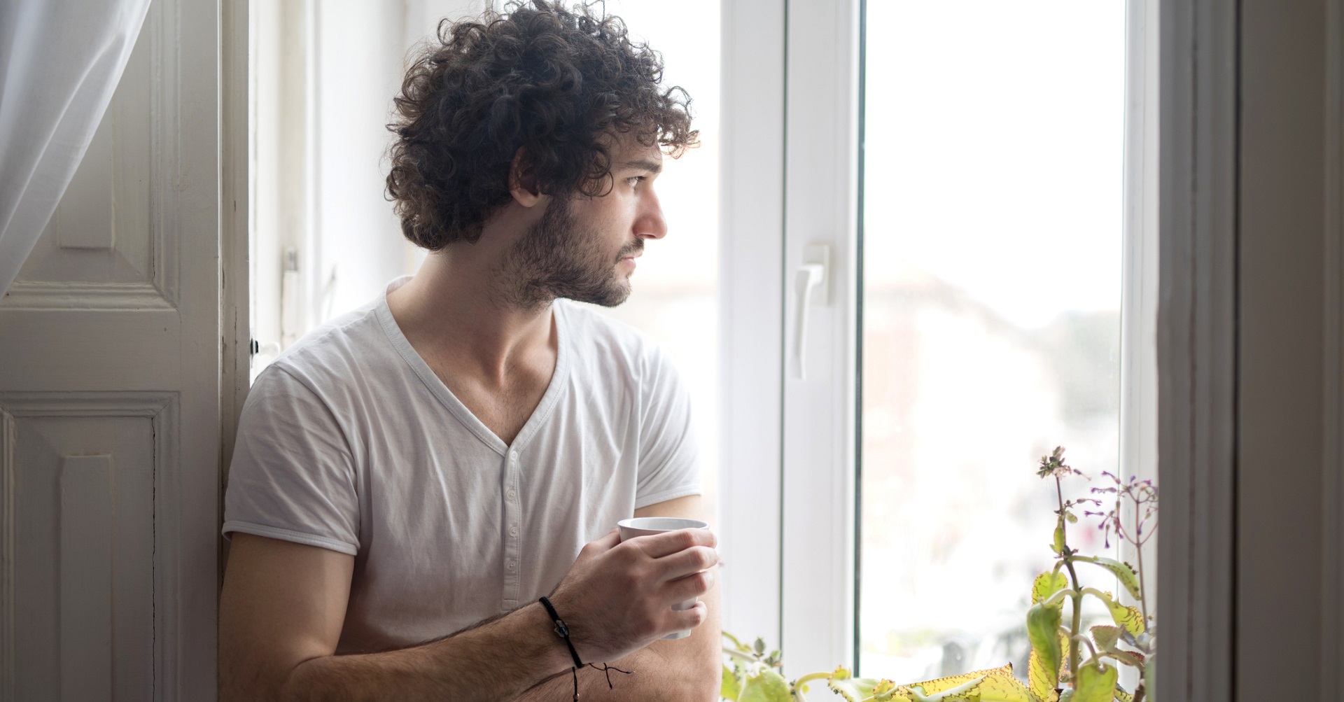man staring out window with cup of coffee